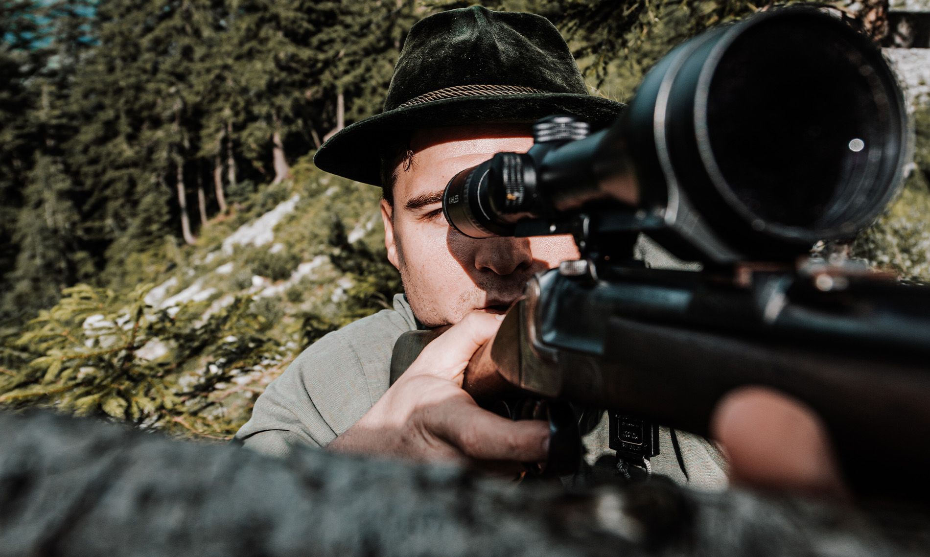 Close-up of hunter’s face focusing through rifle scope in forest, using bachmaier costumfit hearing protection.