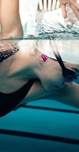 Swimmer wearing custom-fit water protection while swimming underwater in a pool. Custom-fit water protection helps prevent water from entering the ear canal, providing a secure fit and reliable protection for swimming, water sports, training sessions, and regular pool use.
