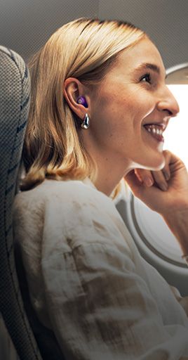 Person wearing custom hearing protection while seated on an airplane next to a window. Custom-fit hearing protection helps reduce cabin noise during air travel, providing greater comfort and a more relaxing journey for frequent travelers and vacation trips.