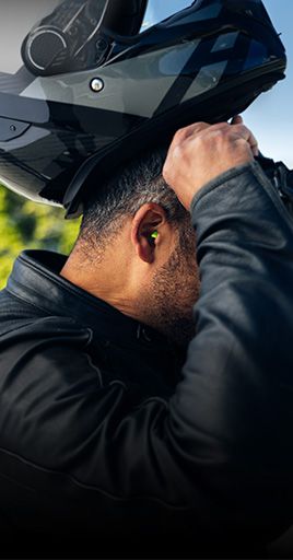 Motorcyclist inserting custom hearing protection before putting on a motorcycle helmet. Custom-fit hearing protection helps reduce wind and engine noise during motorcycle rides while maintaining comfort and protecting hearing on long journeys.