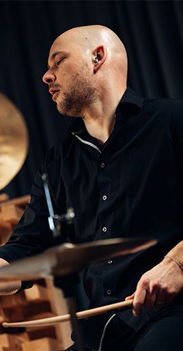 Musician wearing custom hearing protection while playing drums in a studio setting. Custom-fit hearing protection helps reduce exposure to high sound levels while preserving sound clarity, making it ideal for musicians, rehearsals, or recording sessions.