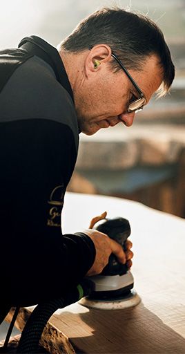 Craftsperson wearing custom hearing protection while sanding a wooden surface in a workshop. Custom-fit hearing protection helps reduce exposure to machinery and tool noise, providing long-lasting comfort and reliable hearing protection for woodworking, craftsmanship, and industrial work environments.