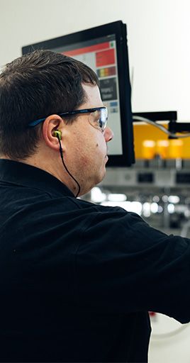 Industrial worker wearing custom hearing protection while operating equipment in a manufacturing environment. Custom-fit hearing protection helps reduce exposure to machine noise while maintaining comfort and situational awareness, making it ideal for industrial workplaces, production facilities, and manufacturing operations.