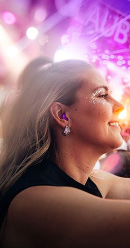 Person wearing custom hearing protection protection at a live music festival, surrounded by colorful stage lights and concert atmosphere. Custom-fit ear protection helps reduce harmful noise levels while preserving sound quality for concerts, festivals, and live events.