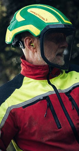 Forestry worker wearing custom hearing protection together with a safety helmet and face shield while operating machinery in a forest environment. Custom-fit hearing protection helps reduce exposure to loud equipment noise, providing reliable hearing protection and long-lasting comfort for forestry, arborist, and outdoor industrial work.